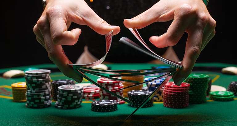 Hands shuffling cards over a poker table