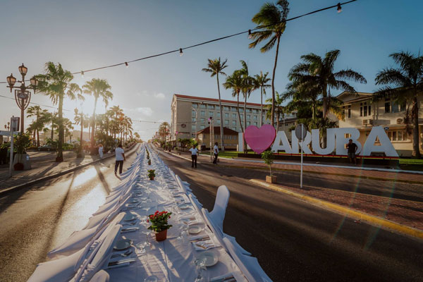 A long table extends down the center of a road and into the horizon. A large I heart Aruba installation is on the right-hand side.